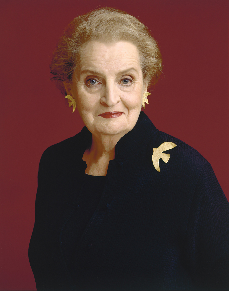 Waist length photo of an older woman in a black suit against a red background