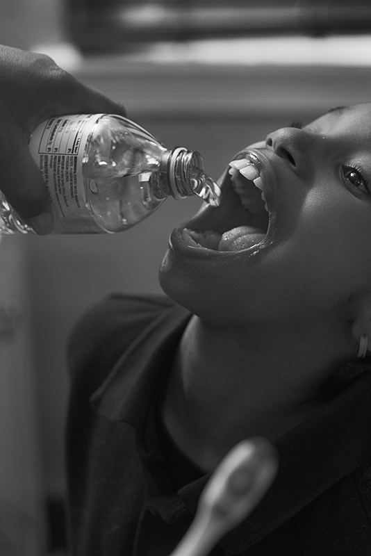 Young child with their mouth open and someone squirting water into their mouth