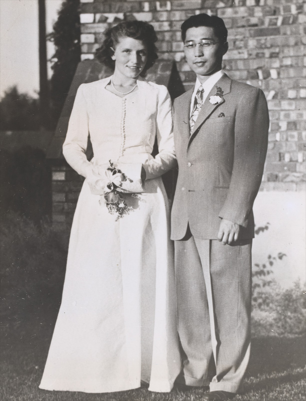 Full length photo of a couple on their wedding day.  the woman is White the man, Asian