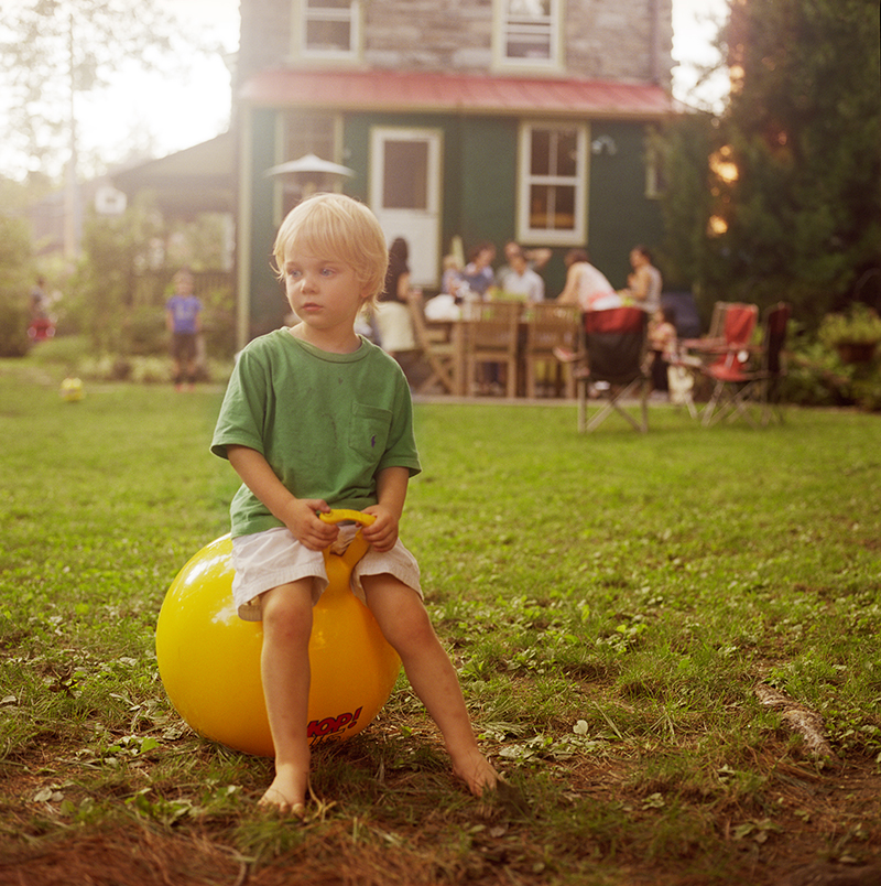 small boy on a yellow ball in a yard with family members
