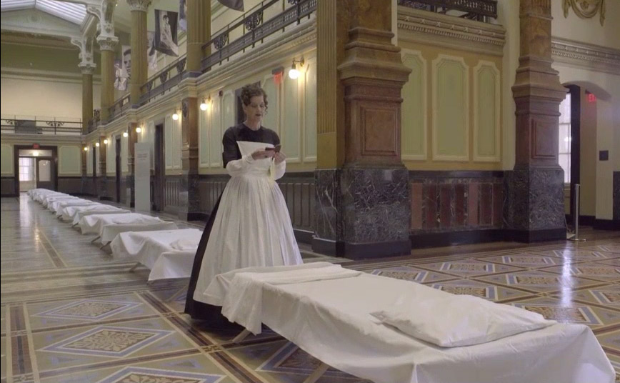 woman in 19th century dress coveribg cots with sheets