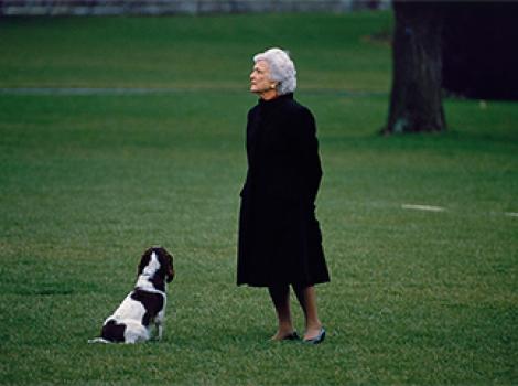 Woman in a black coat standing on a green lawn with a dog