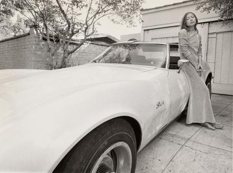 A black and white image of a woman leaning against a car