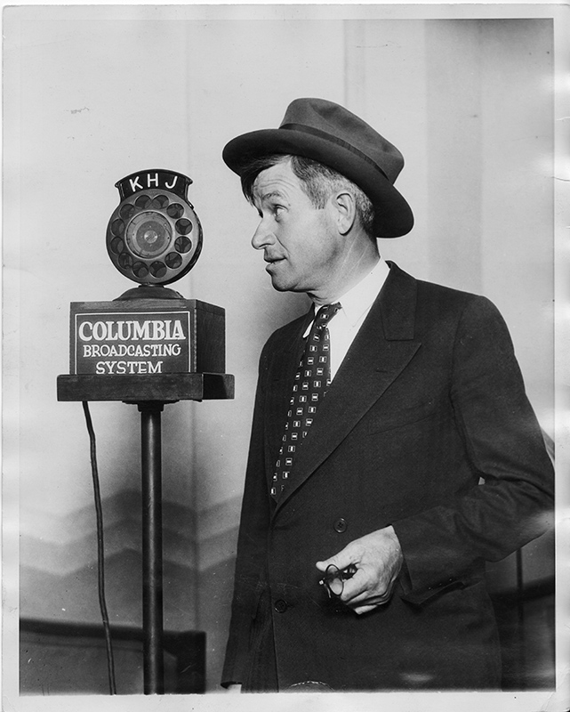 man in a suit and a hat speaking into a microphone
