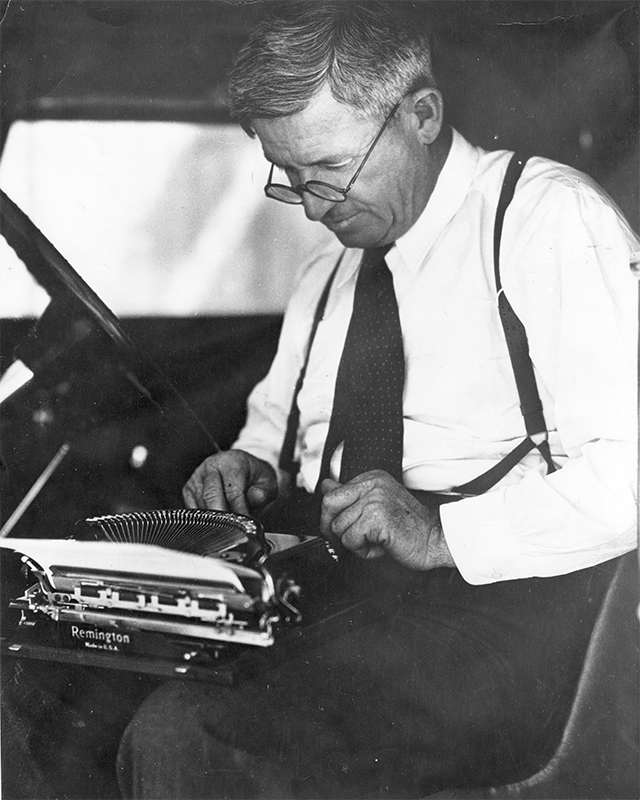 man in a suit working at a typewriter while sitting in a car